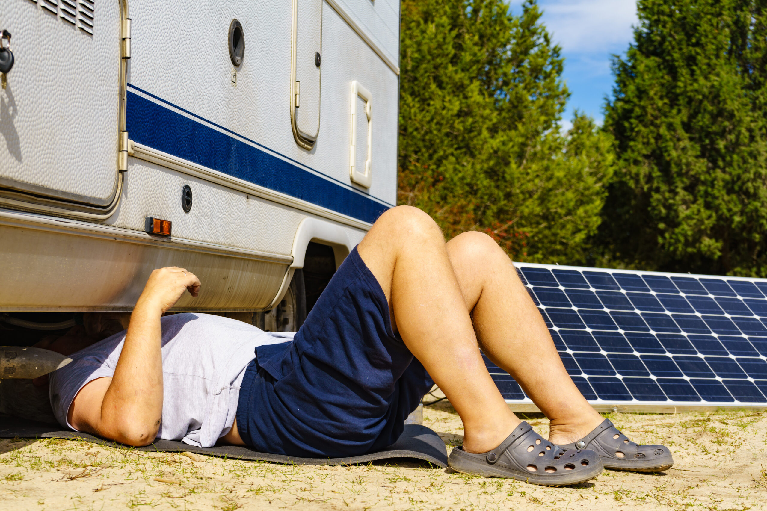 Man lying on ground, repairing bottom of the caravan vehicle.